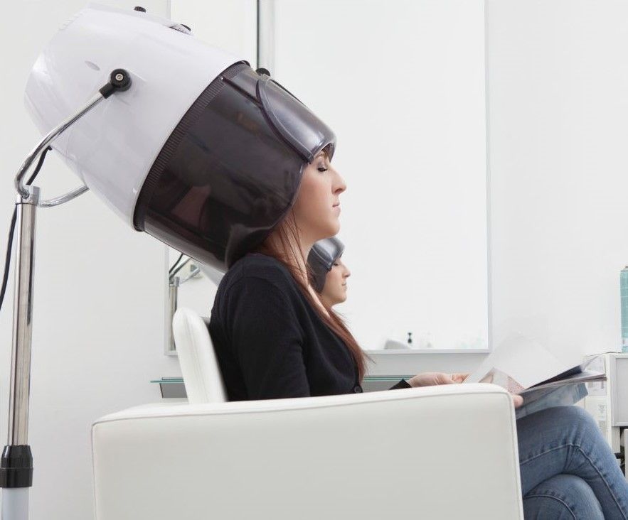 A woman is sitting in a chair with a hair dryer on her head.