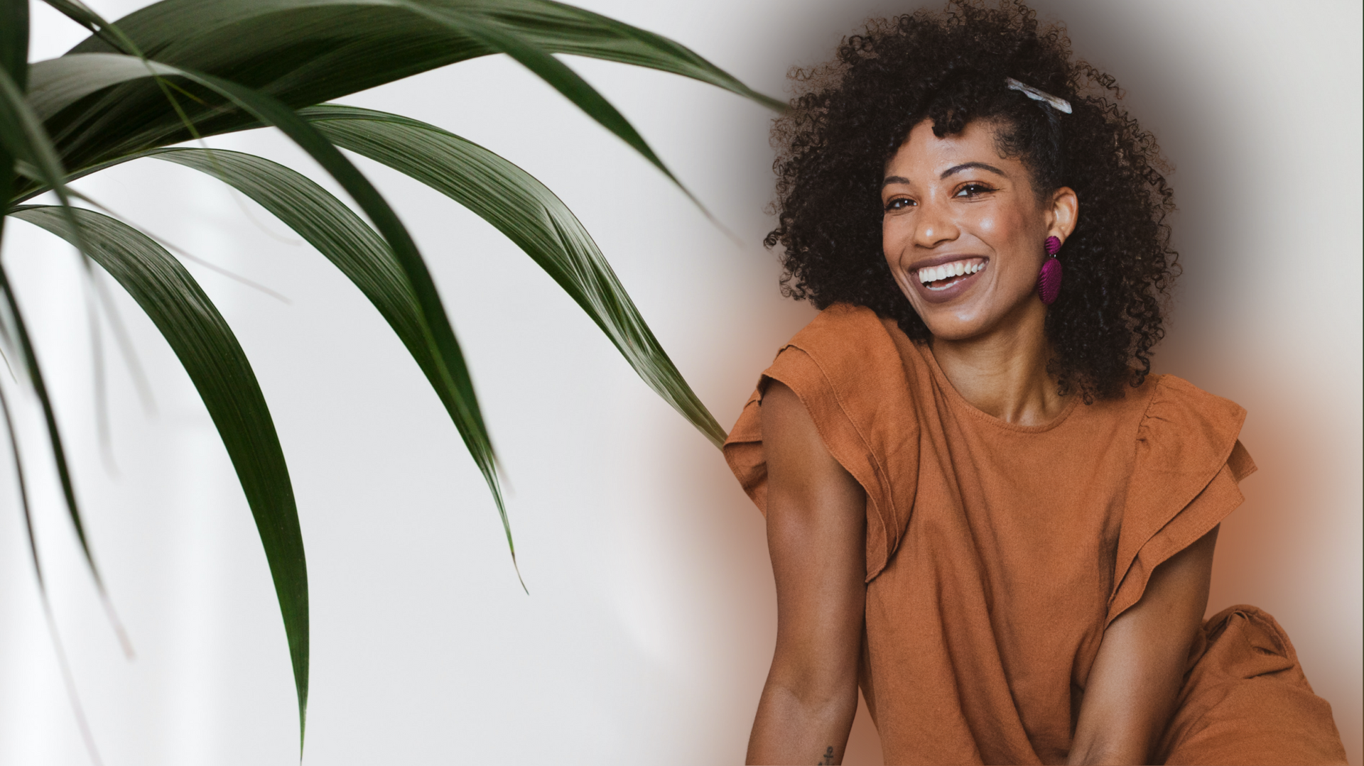 A woman in a brown dress is smiling in front of a palm tree.