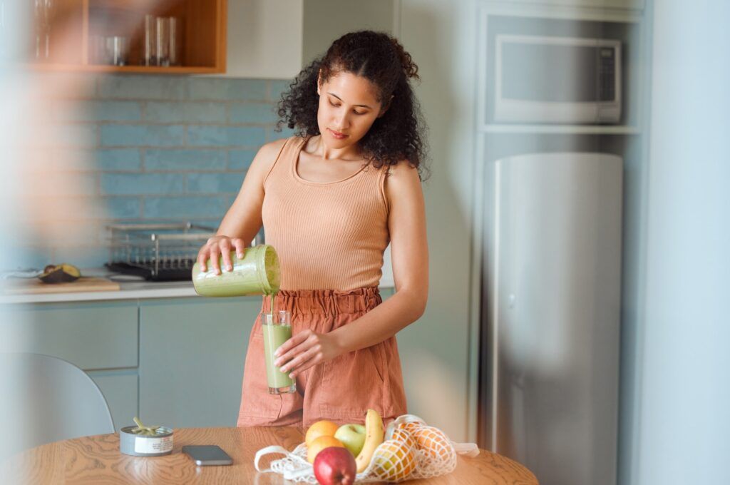 A woman is pouring a green smoothie into a glass.