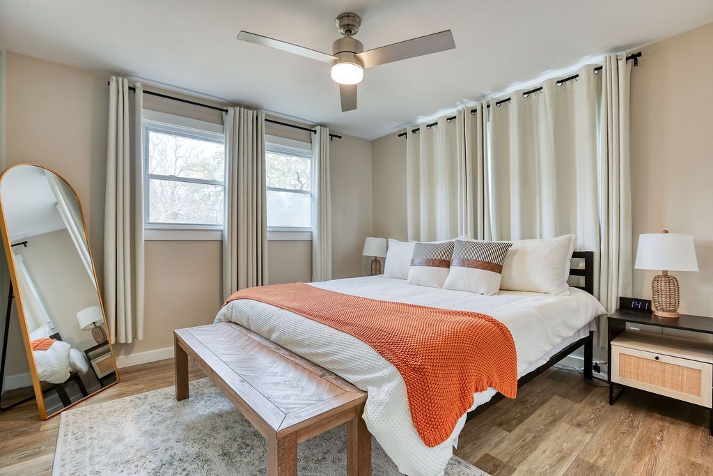 A bedroom with a large bed , a bench , a mirror and a ceiling fan.