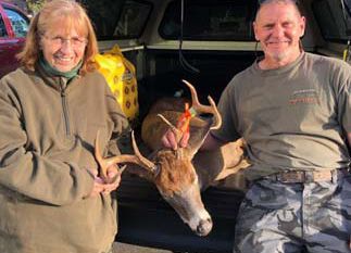 A man and a woman are holding a deer in the back of a truck.
