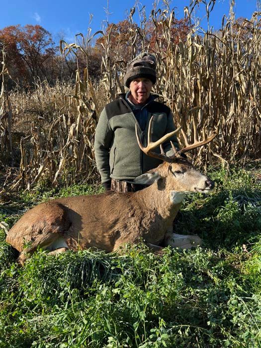 A man is standing next to a deer in a field of corn.