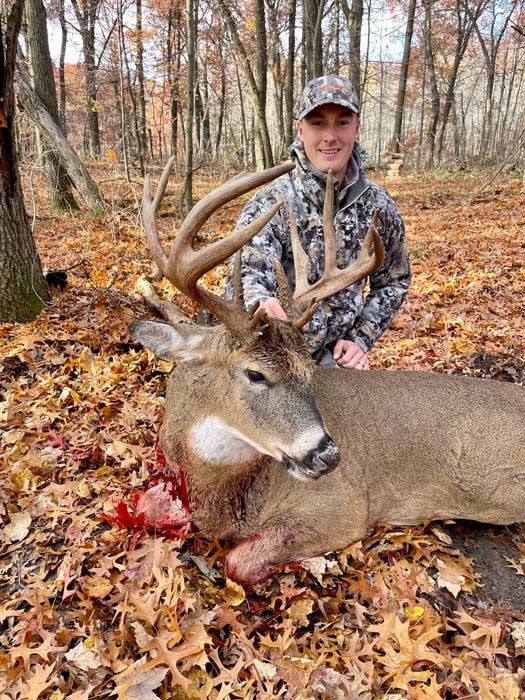 A man is standing next to a deer in the woods.