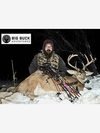 A man is standing next to a large deer in the snow.