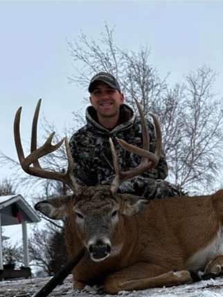 A man is standing next to a large deer in the snow.