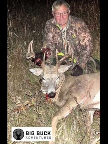Hunter lifting a deer’s body with a proud smile in the woods