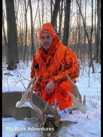 A man in an orange jacket is kneeling next to a deer in the snow.