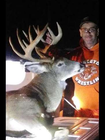 A man in an orange shirt is standing next to a large deer.