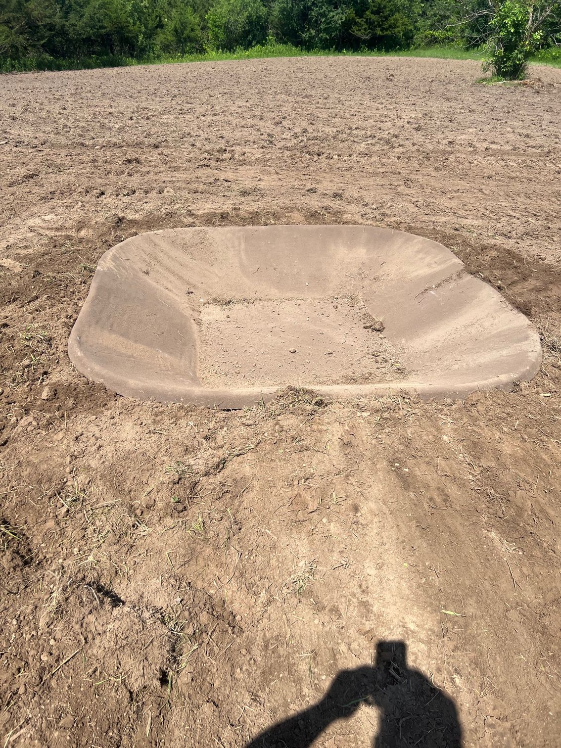 A wheelbarrow is sitting in the middle of a dirt field.