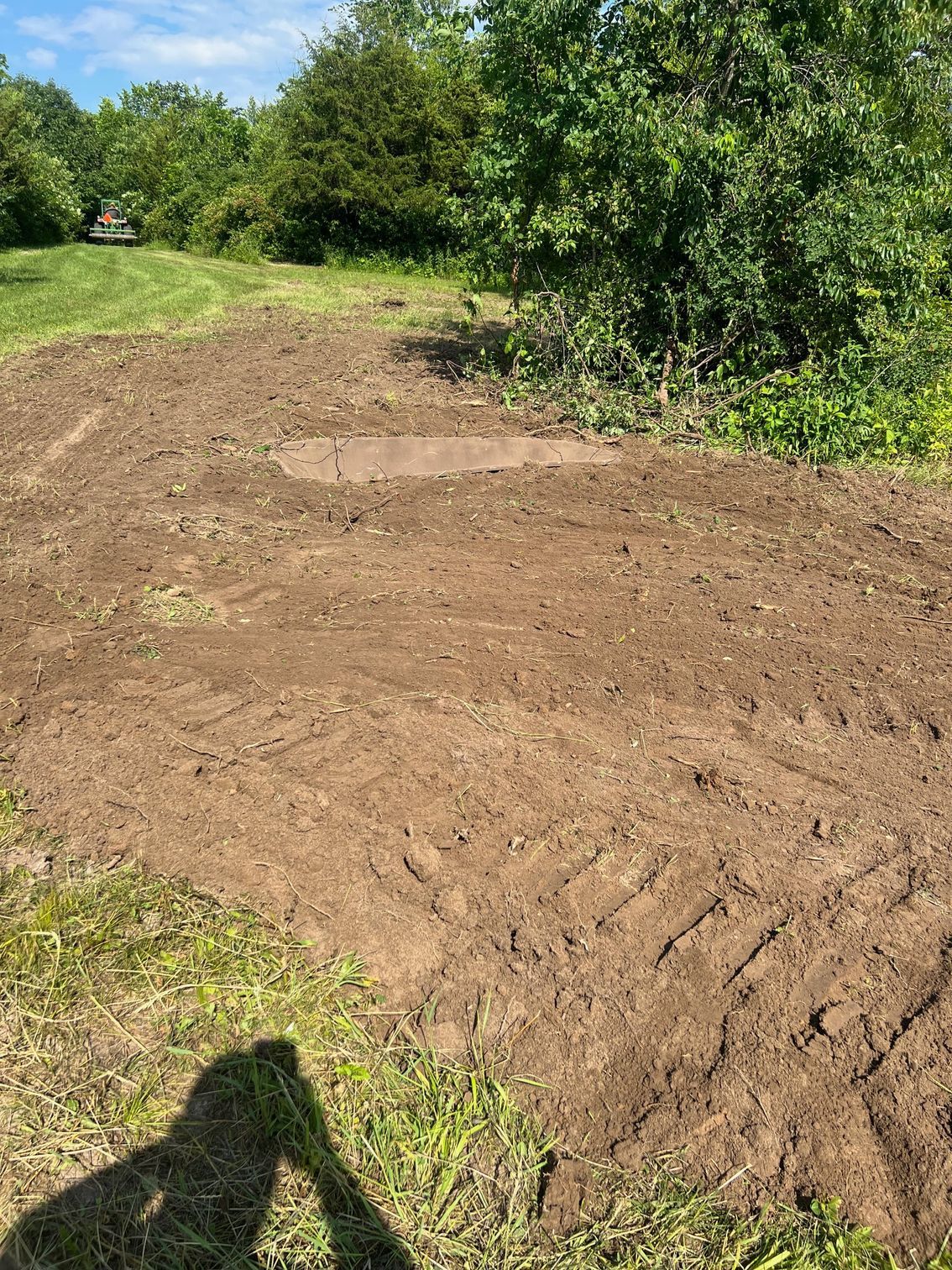 A large pile of dirt in a field with trees in the background.