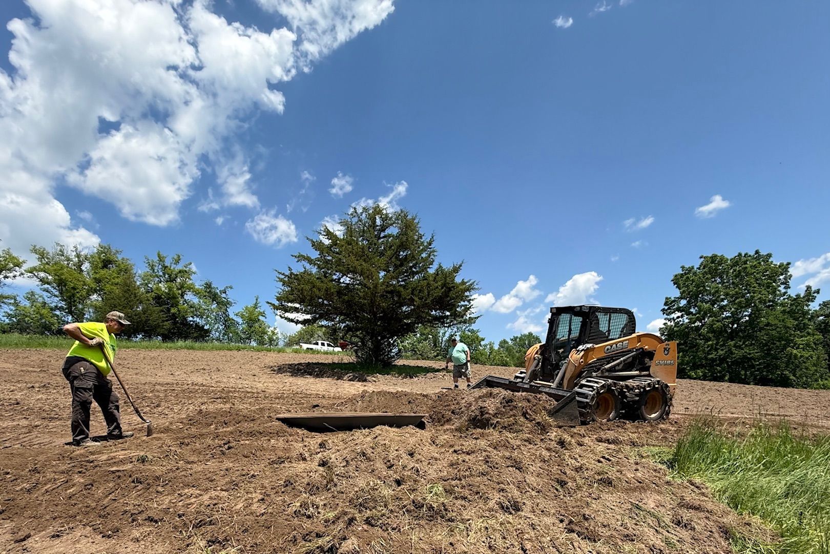 A man is digging in a field with a tractor in the background.