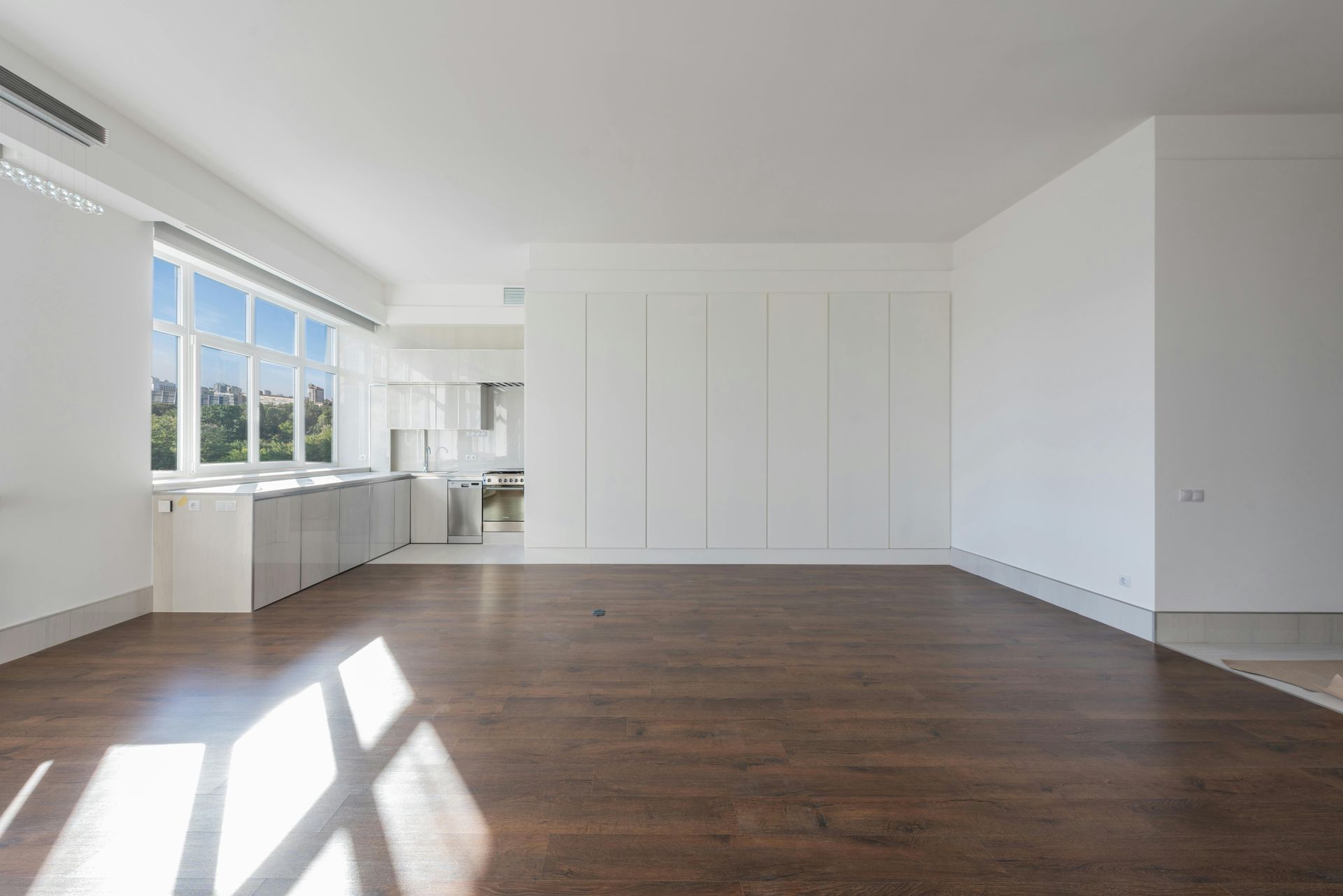 Empty, bright room with hardwood floor, white walls, and a large window.