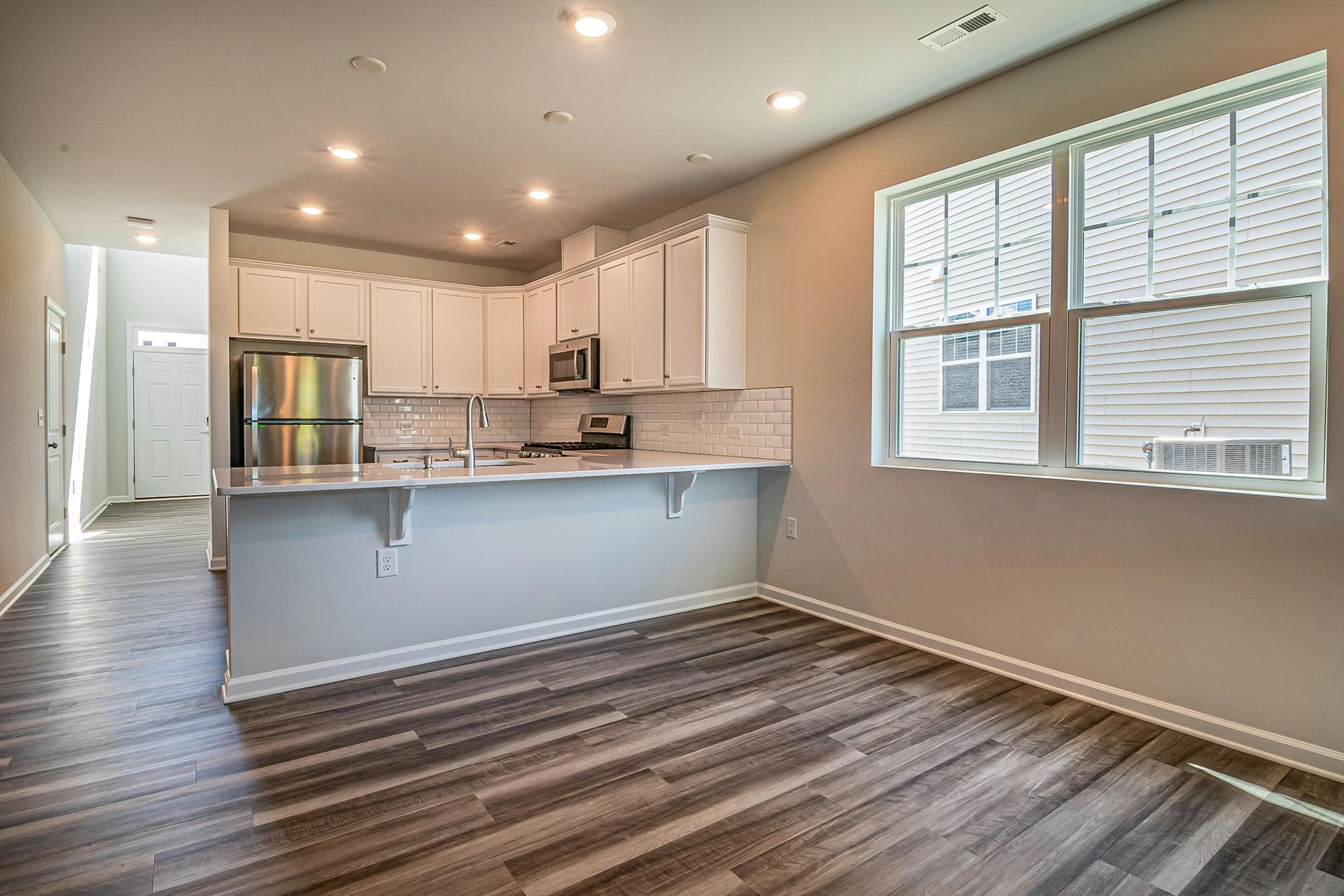 Open-concept kitchen with white cabinets, stainless steel appliances, and a gray-brown wood floor.