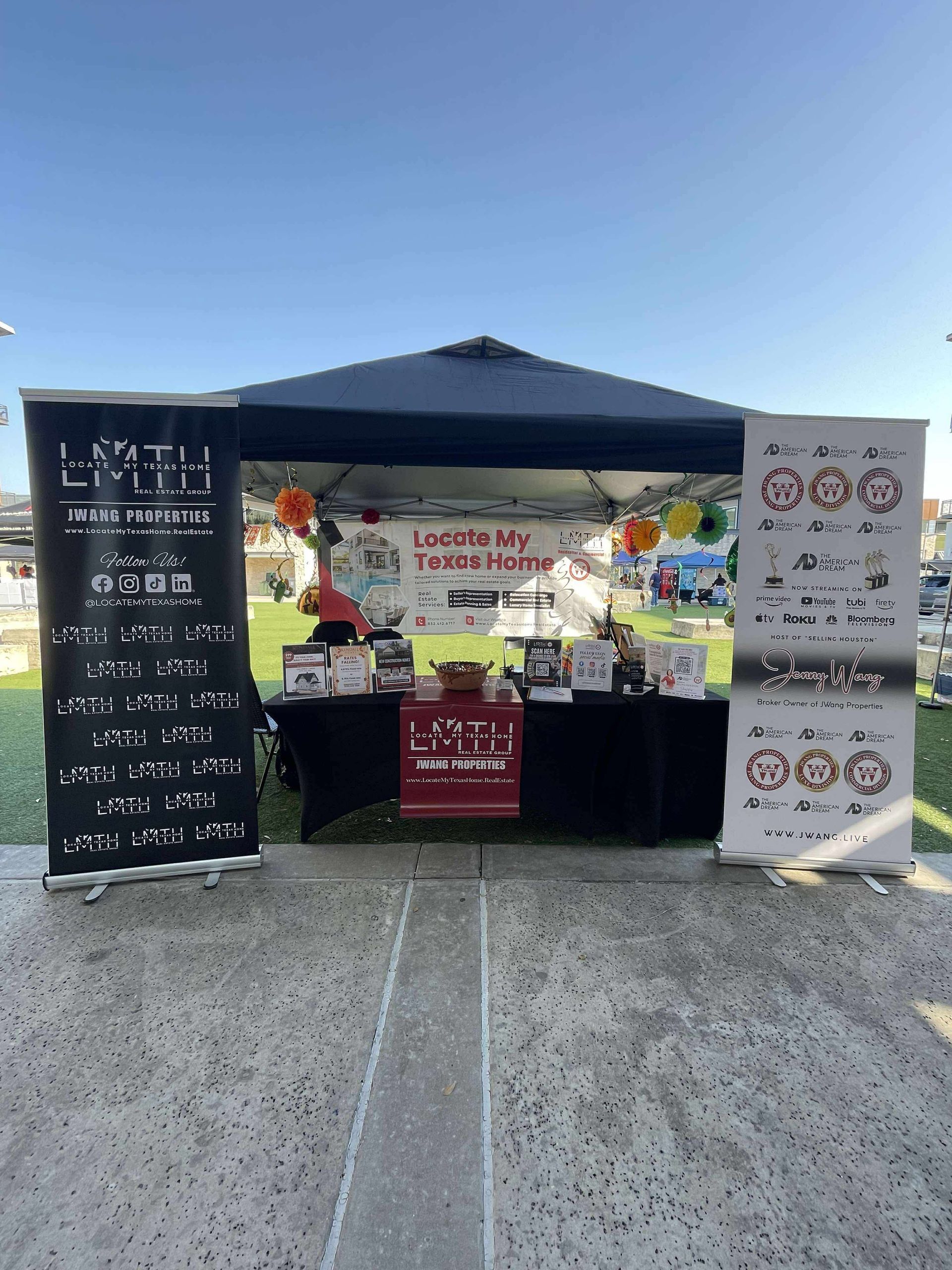 A vendor booth at an outdoor event with signs and various products displayed on a table.