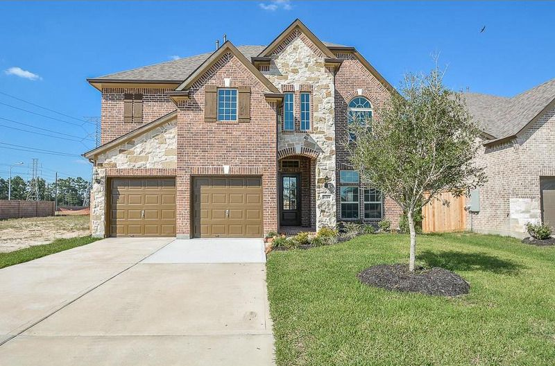 Two-story brick house with stone accents, brown garage doors, and a green lawn on a sunny day.