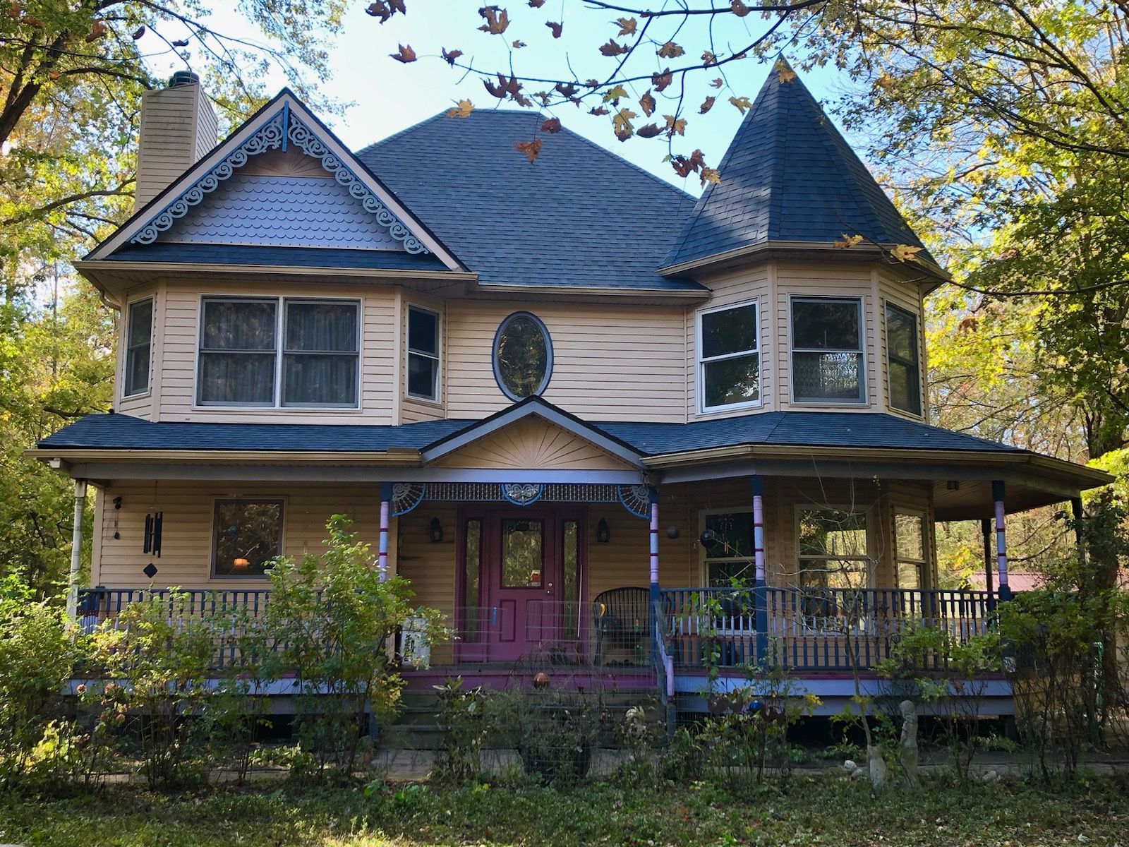 Victorian house with a turret and wraparound porch; light yellow siding, purple trim, and dark blue roof.