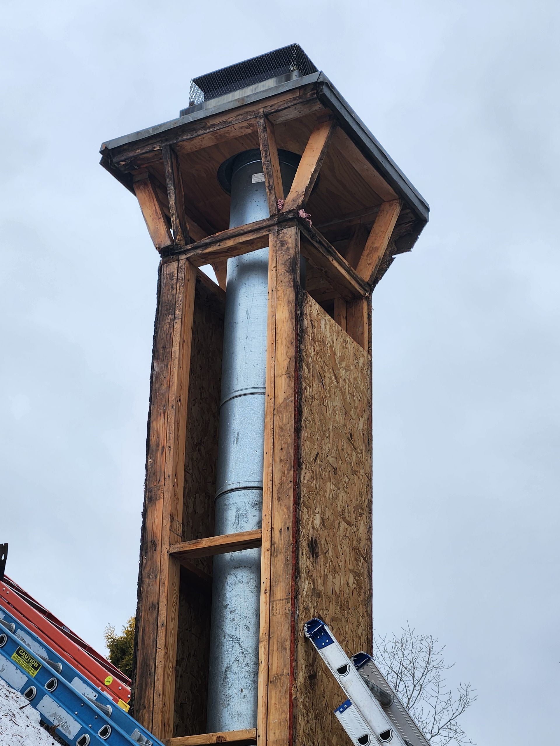 Chimney under construction with a metal flue inside a wood frame structure, on a rooftop.
