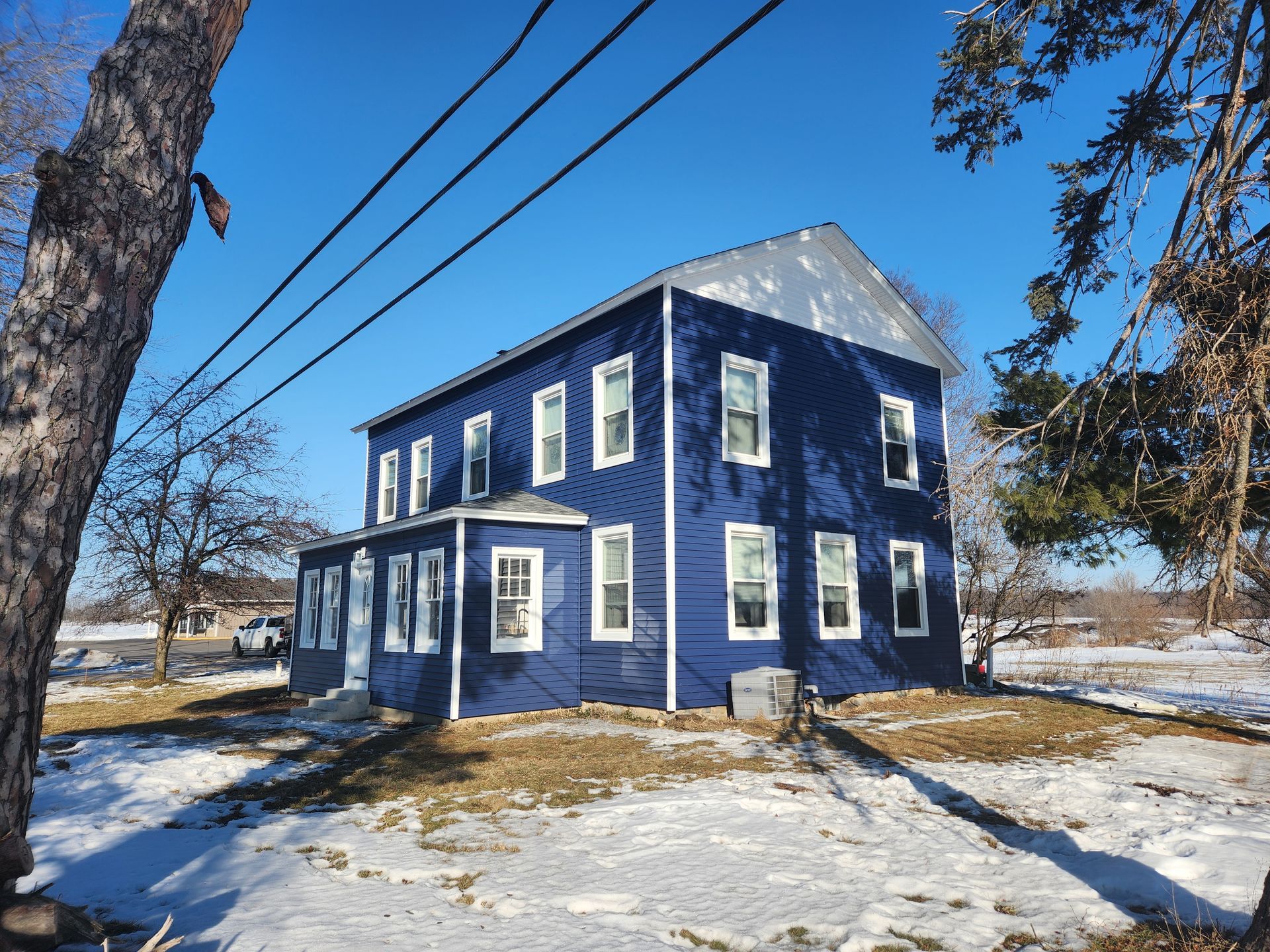 Blue two-story house with white trim on a snowy day. Power lines and bare trees in the frame.