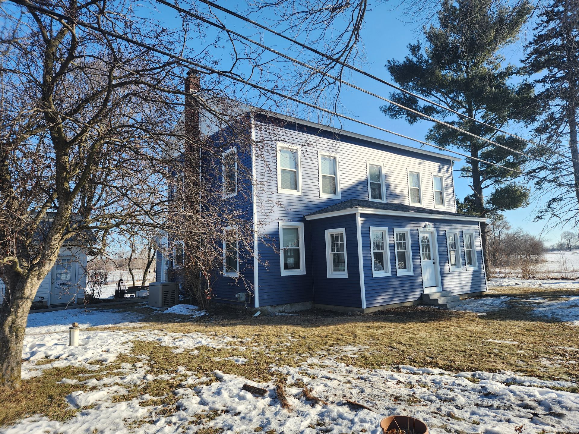 Blue two-story house with white trim in a snowy field on a sunny day.