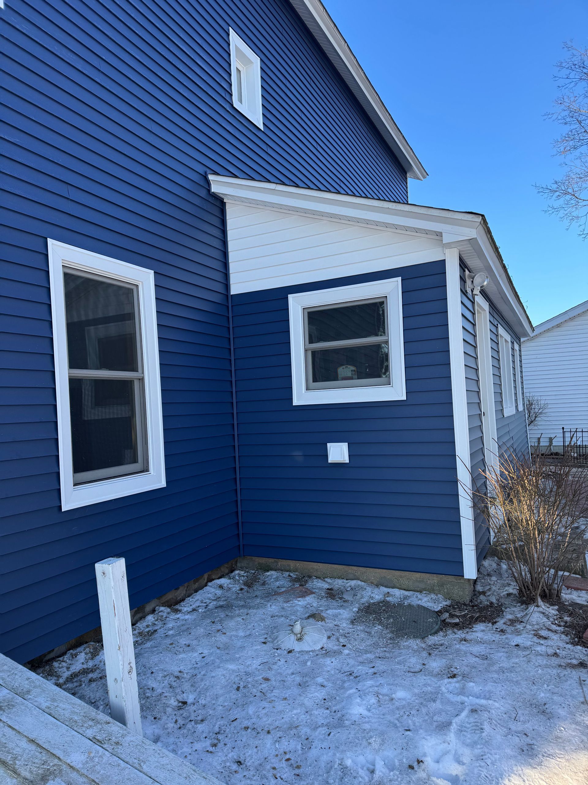 Blue house exterior with white trim, two windows, and snow on the ground.