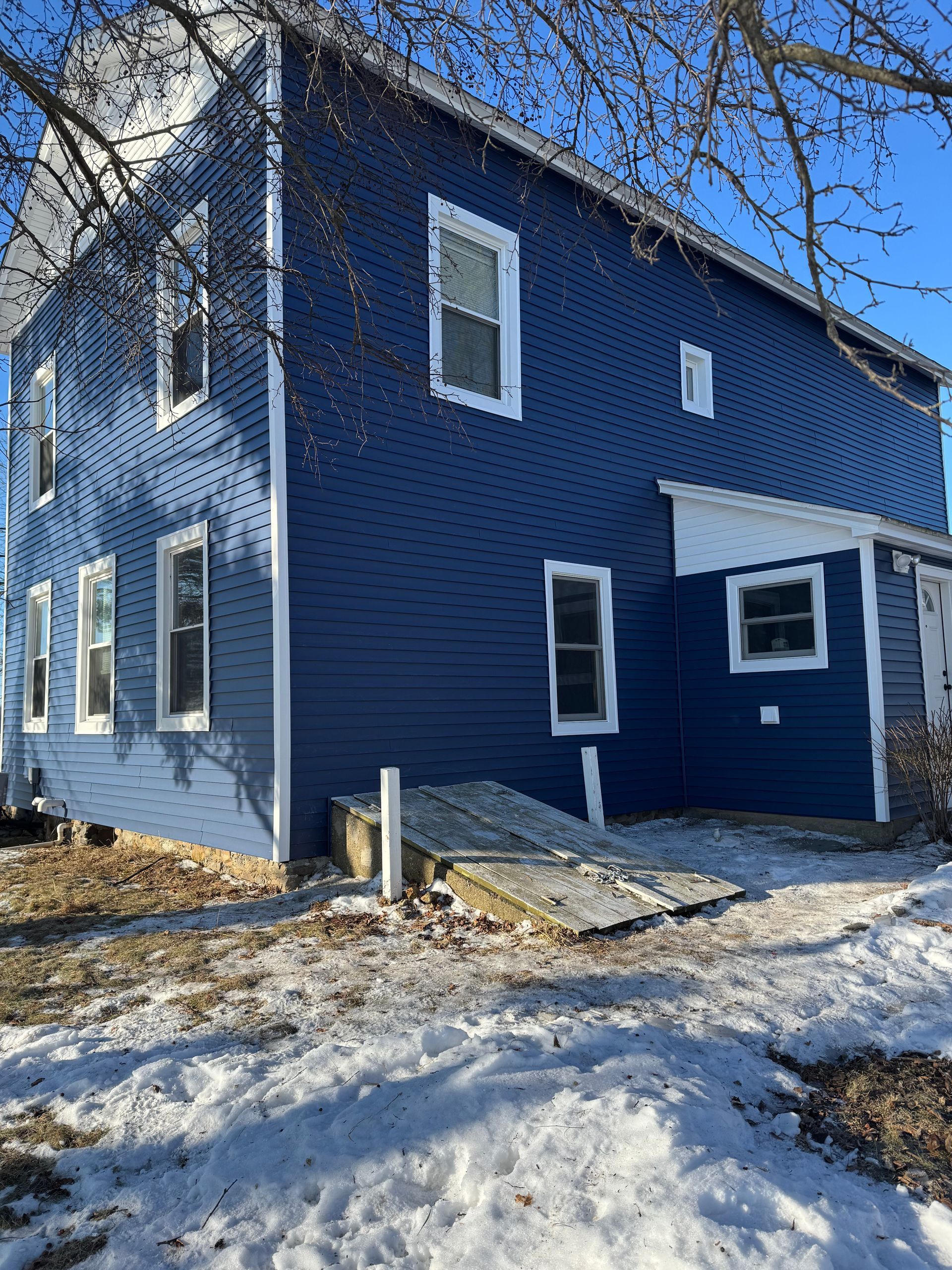 Blue two-story house with white trim and windows. A snow-covered yard surrounds the structure.