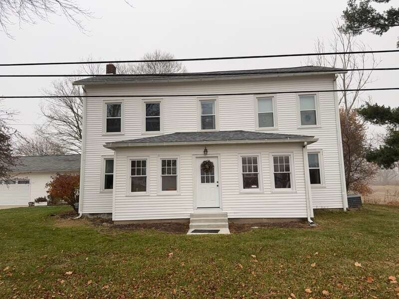 White two-story house with a porch, set on a grassy lawn under an overcast sky.