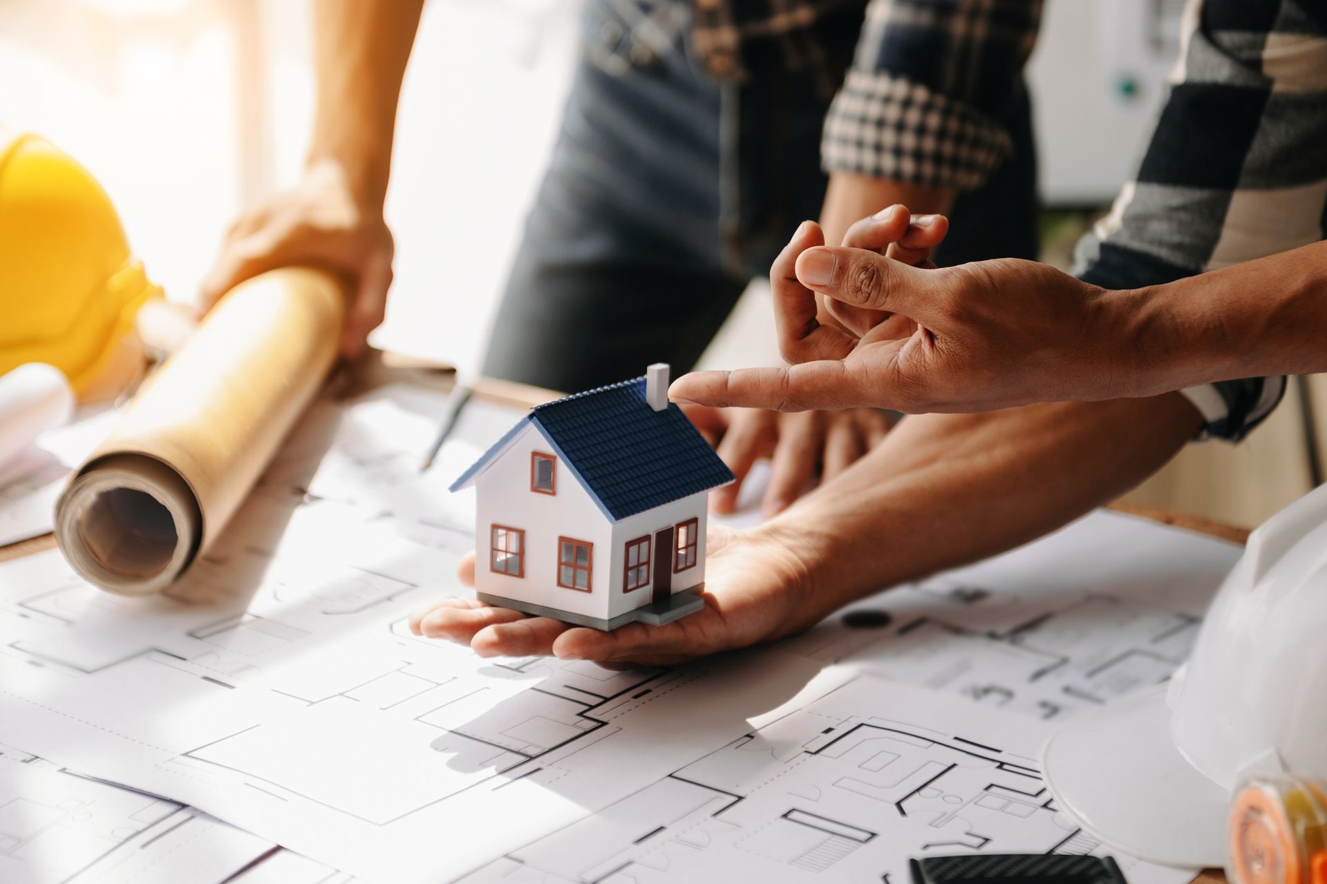 Architects reviewing blueprints around a miniature house model on a desk.