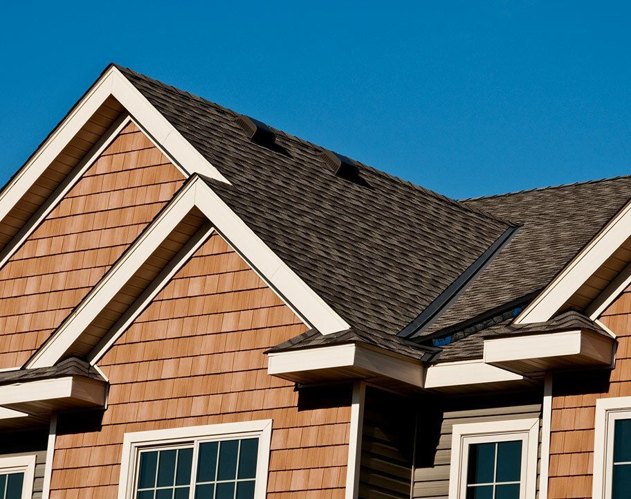 Slate roof with a dark gray chimney against a blue sky with white clouds.