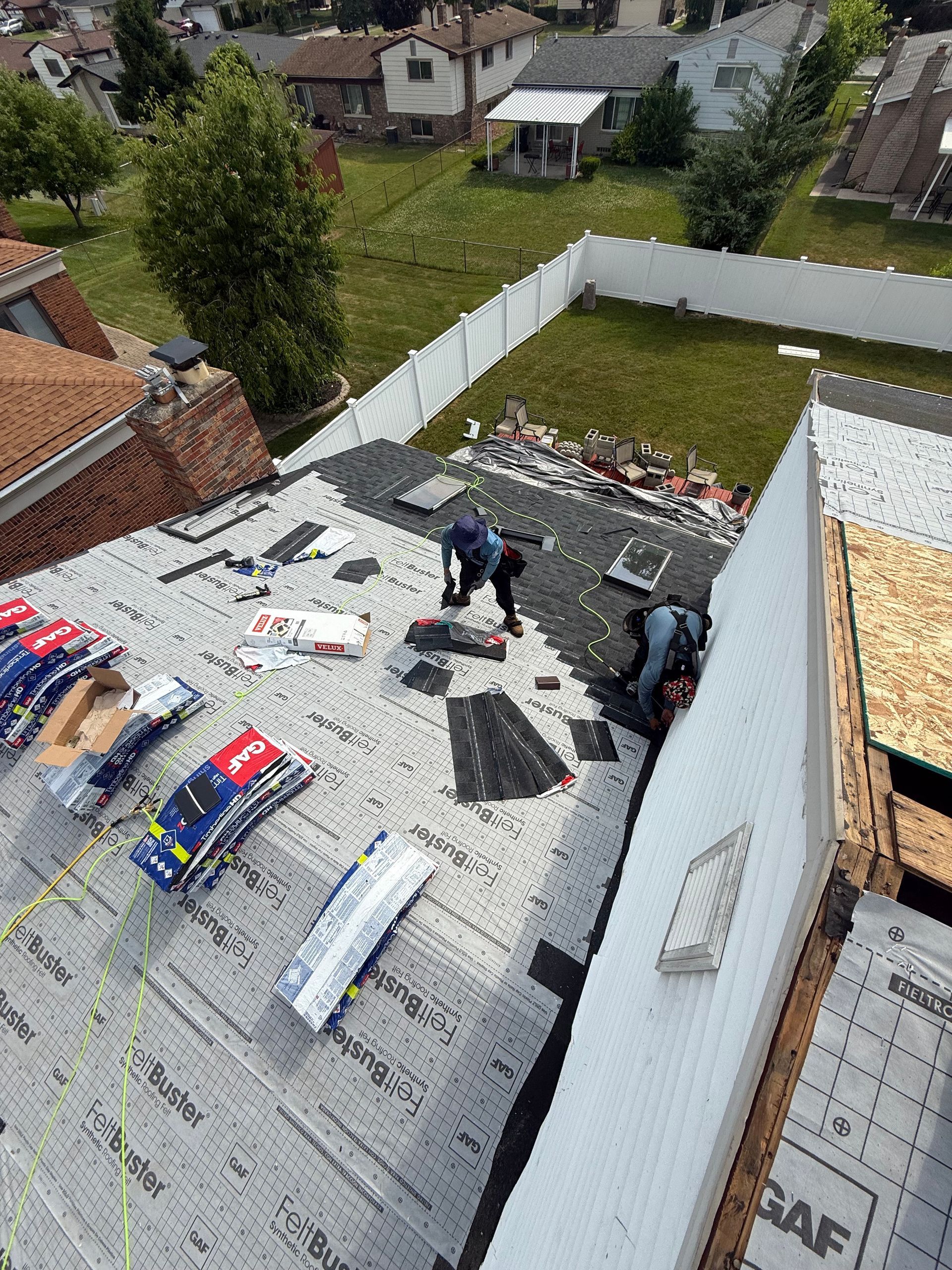 Roofer repairs a damaged shingle roof on a house under a blue sky.