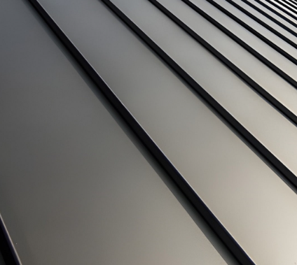 Two construction workers in safety gear installing a dark metal roof on a building under a clear sky