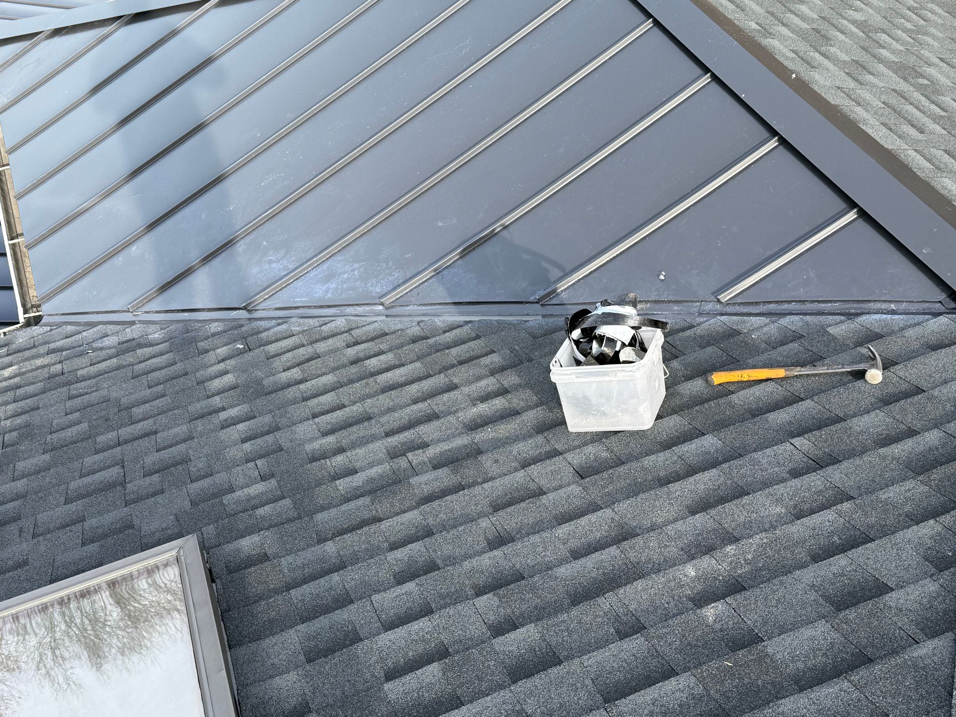 Roofer installing corrugated metal roofing on a partially constructed building. Bright sky with a setting sun is in the background.