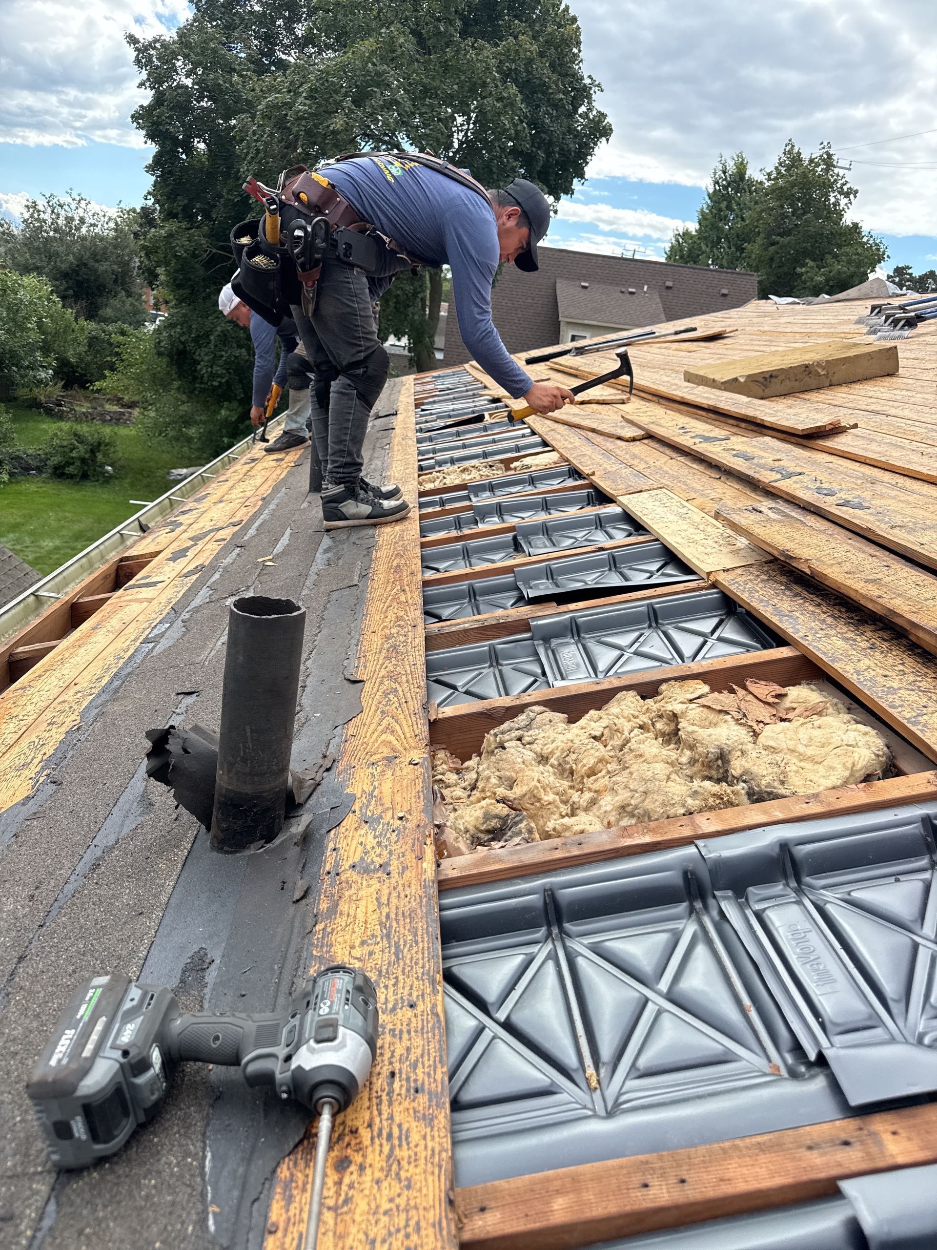 Interior of an unfinished attic with wooden rafters and beams, boards on the floor, and a window in the back.
