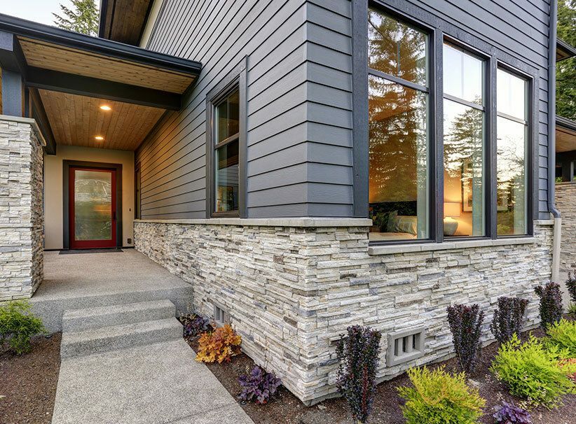 A person's hand installing tan vinyl siding on a house, showing the process and materials.