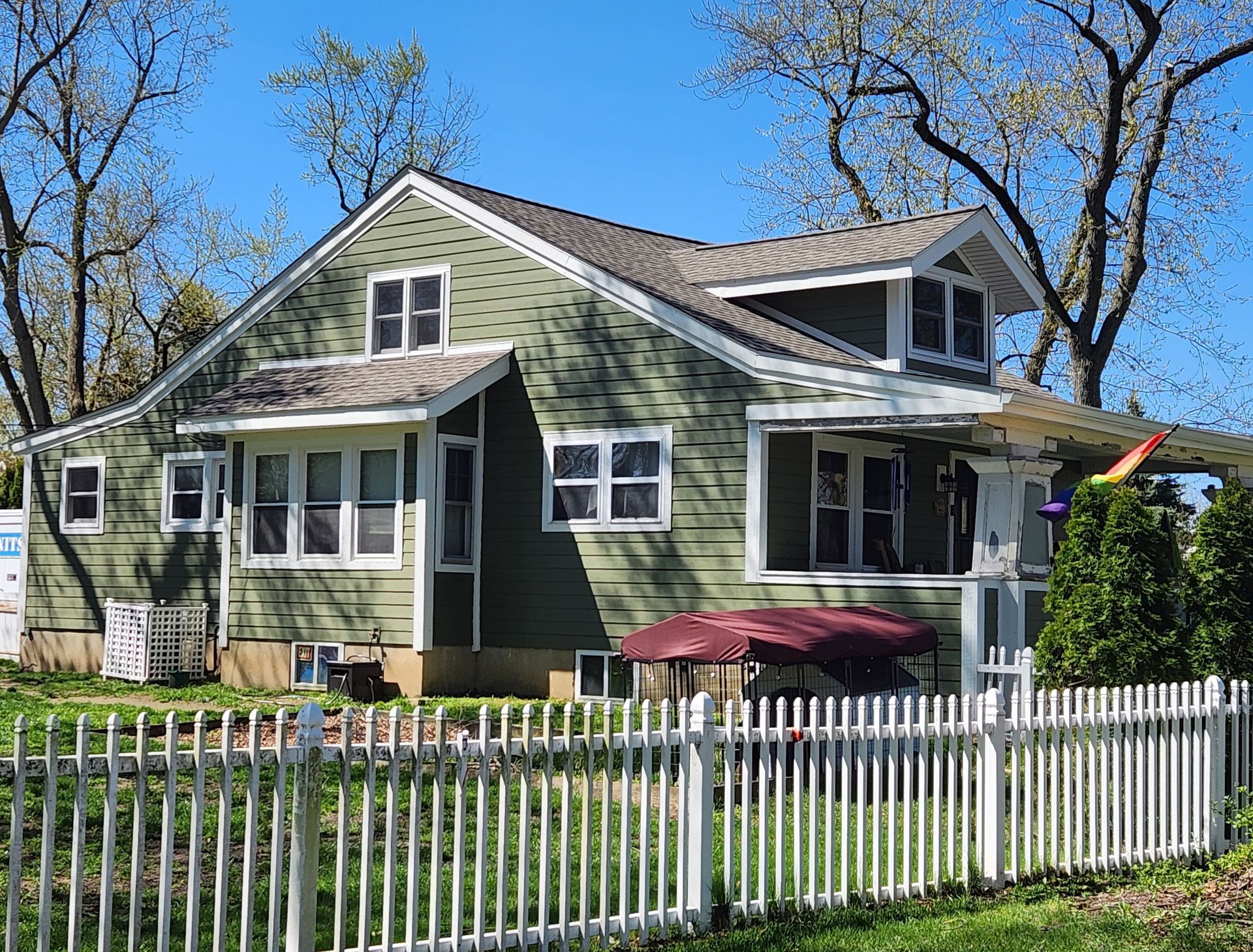 A tan-sided house under construction with a window, dark brown trim, and a blue sky background. Scaffolding visible.