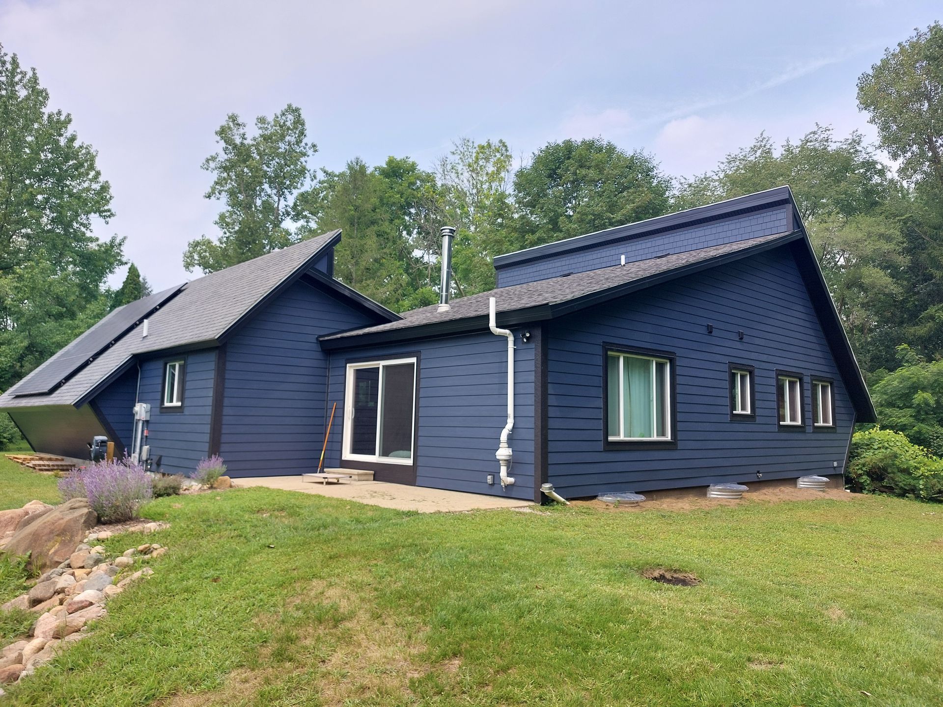 A person in a plaid shirt installs siding on a house exterior with brown and white elements.