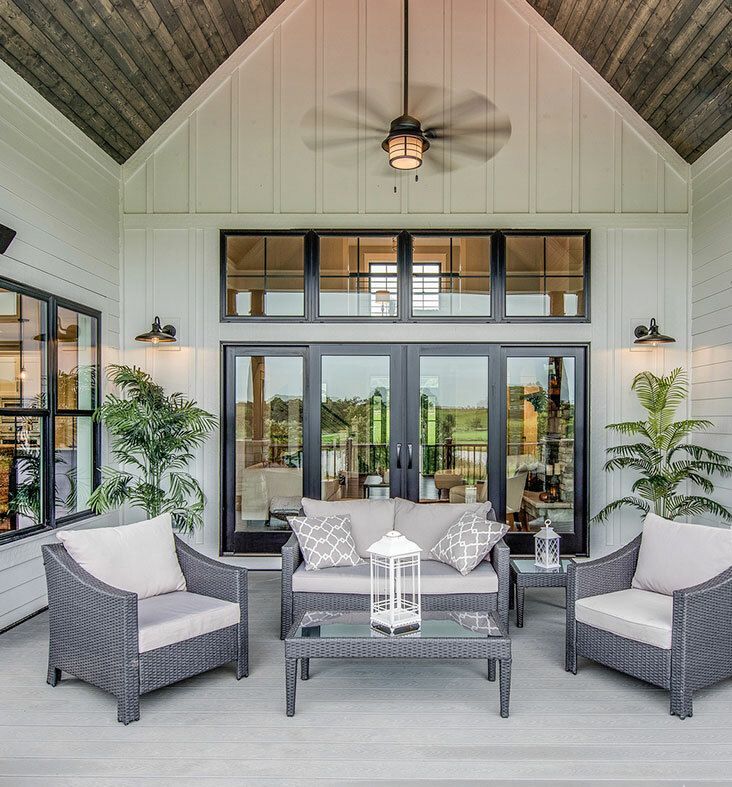 Two people in hard hats review building plans outdoors next to a light-colored house with a dark roof. One person points.