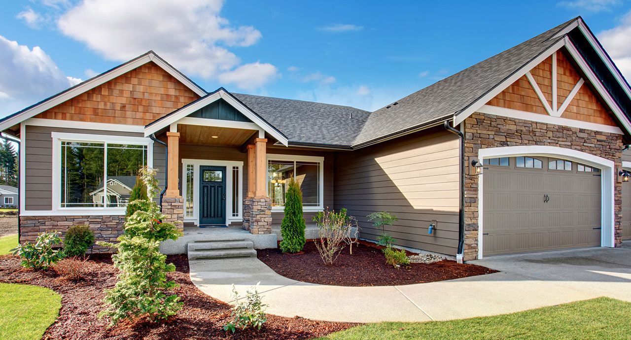 Brown, modern home with a light blue door, garage, and a paved walkway on a sunny day. Landscaping includes shrubs and brown mulch.