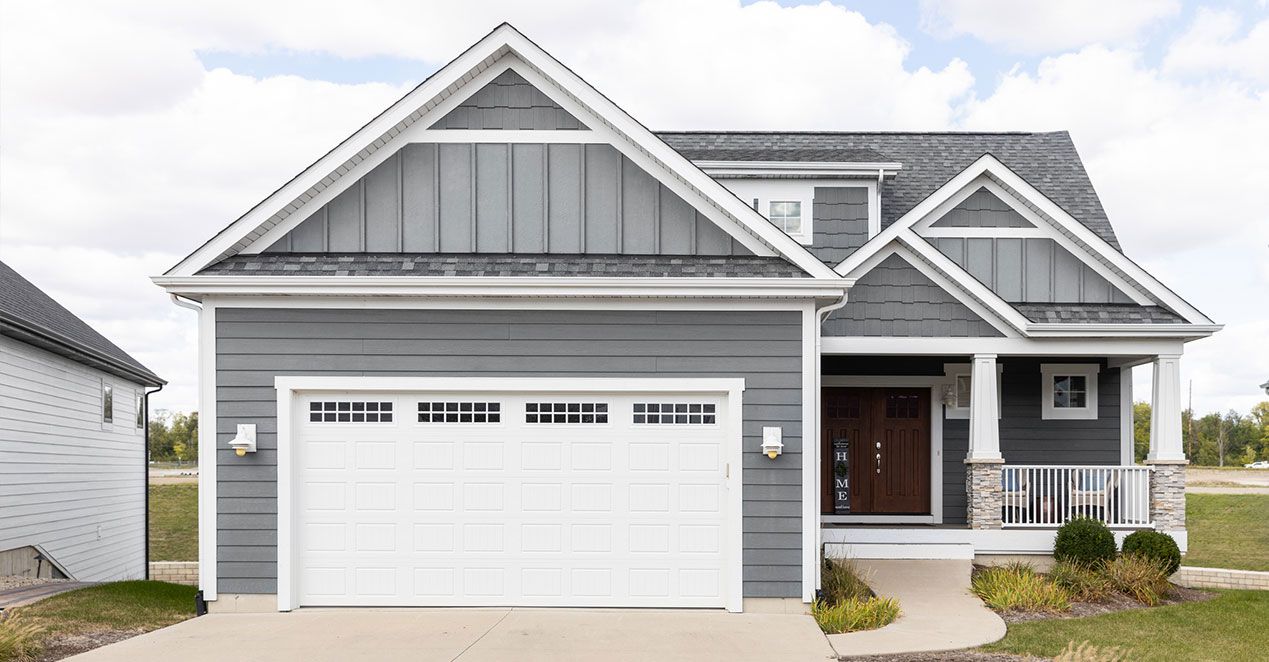 A gray two-story house with a white garage door and a small porch, set against a cloudy sky.