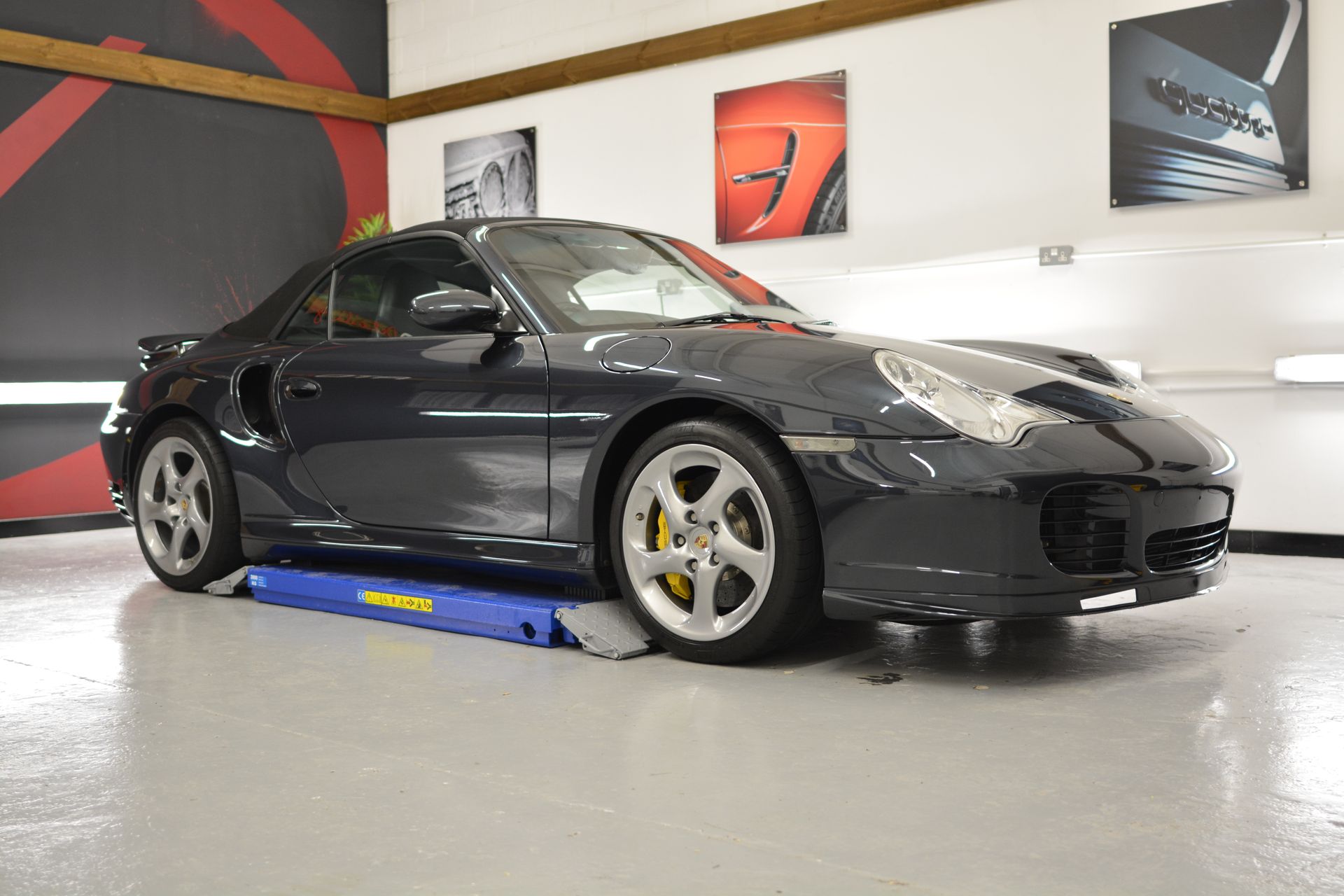 A black sports car is parked on a ramp in a garage.