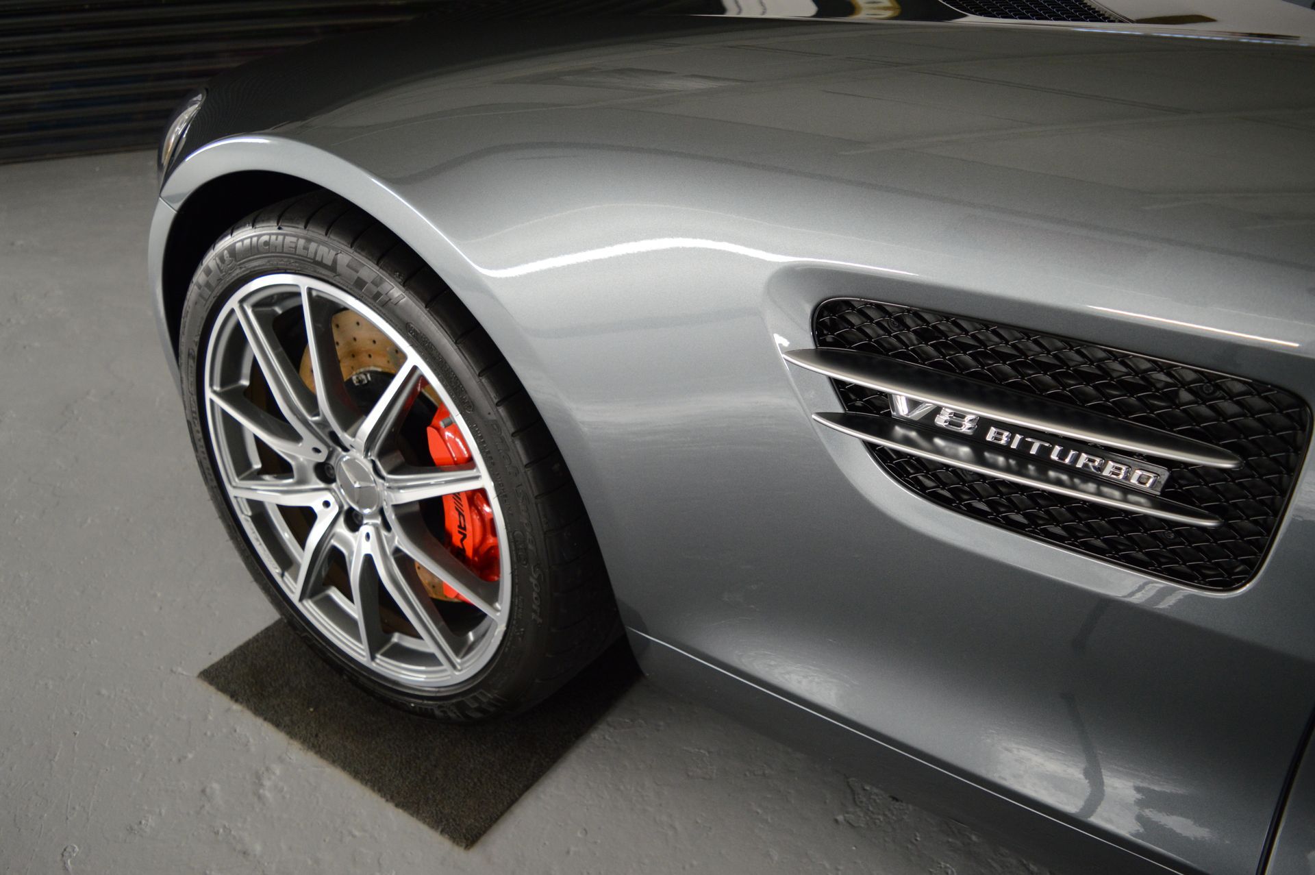 A silver sports car with red brake calipers is parked in a garage.