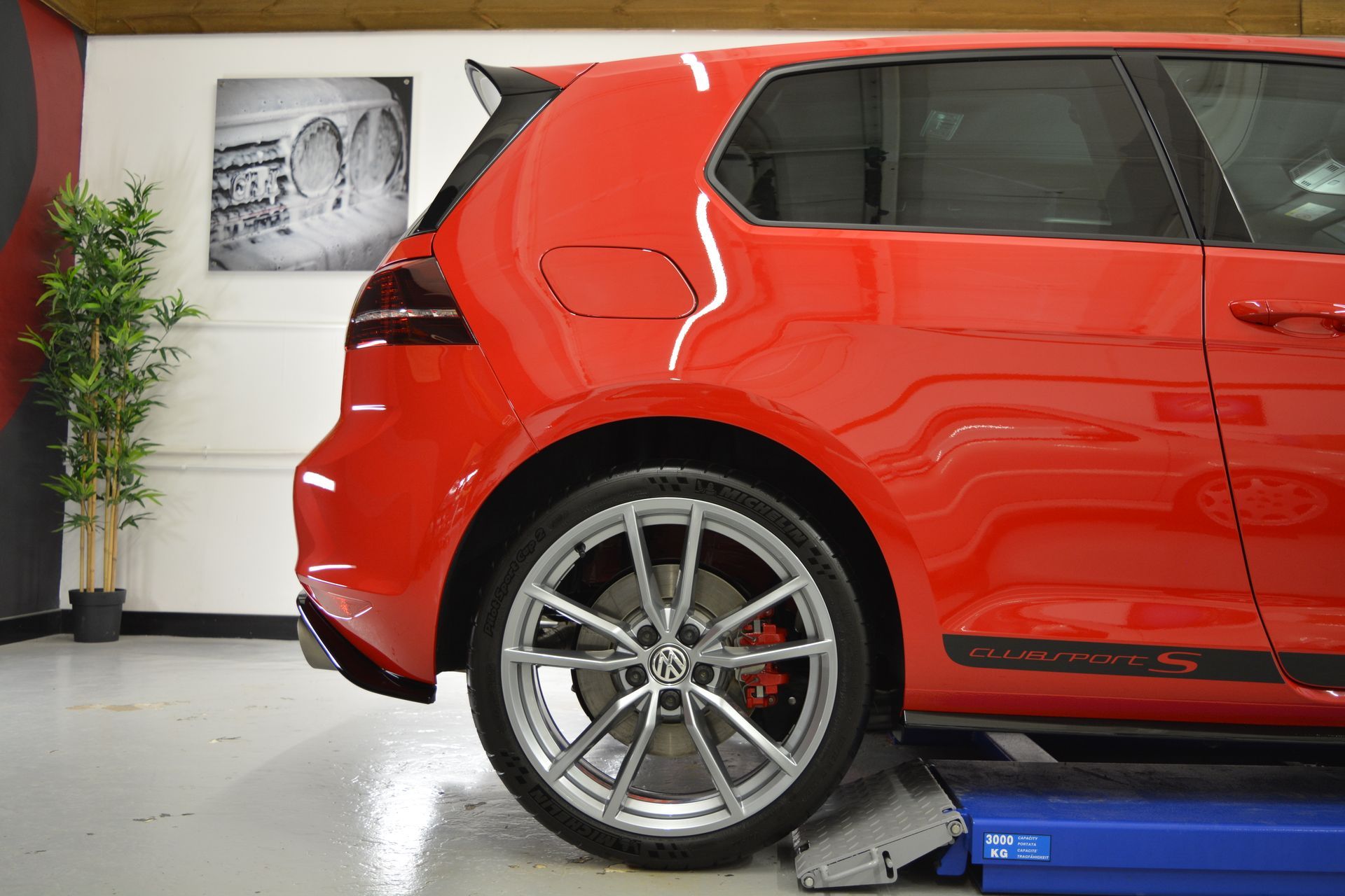 A red car is sitting on a lift in a garage.
