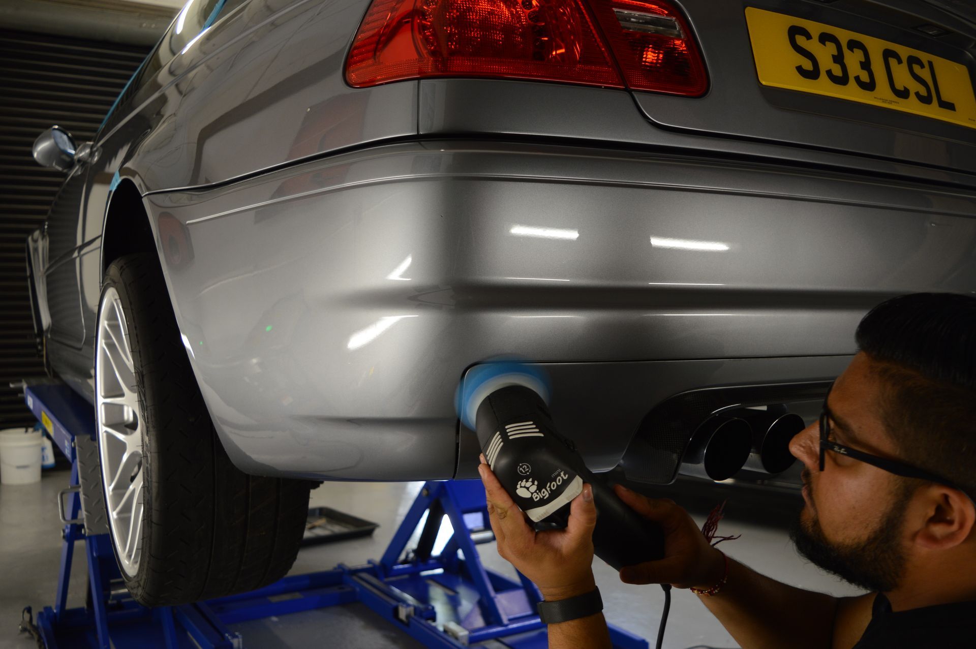A man is polishing the bumper of a car with a machine.