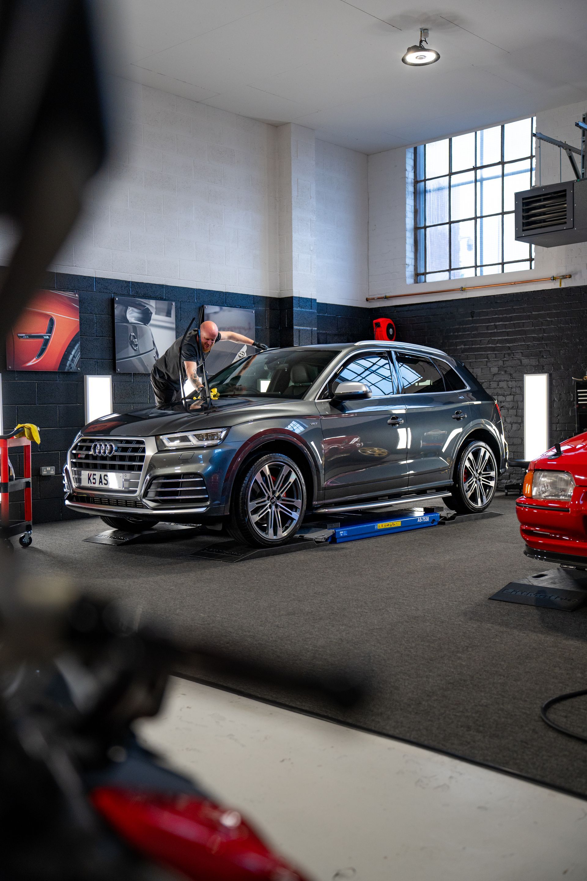 A man is cleaning the windshield of a car in a garage.