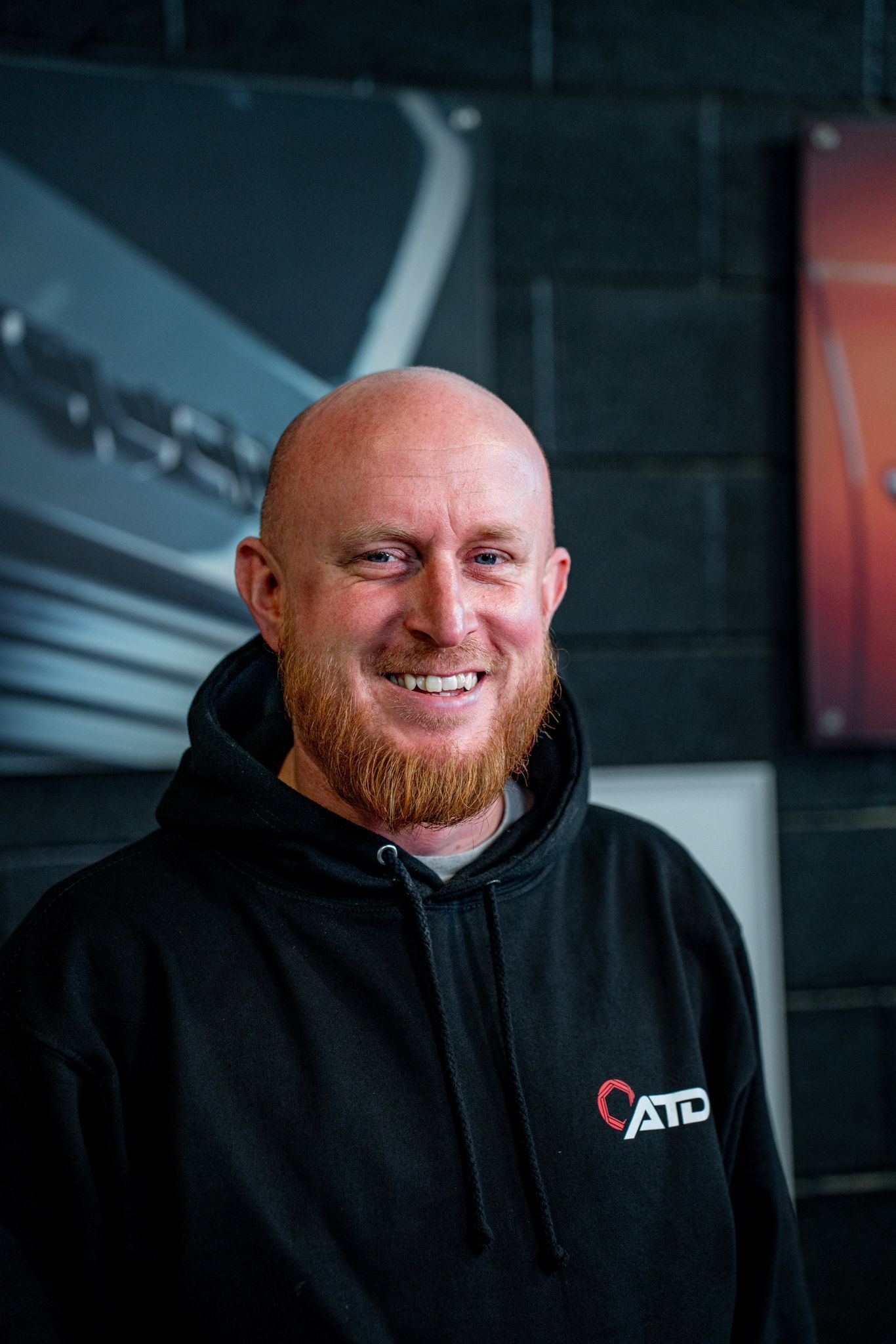 A bald man with a beard is wearing a black hoodie and smiling.