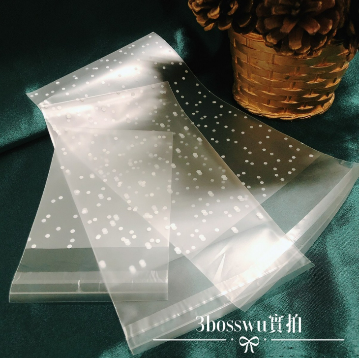 幾個帶有白色波點圖案的半透明自黏塑膠袋排列在深綠色的布料表面上。