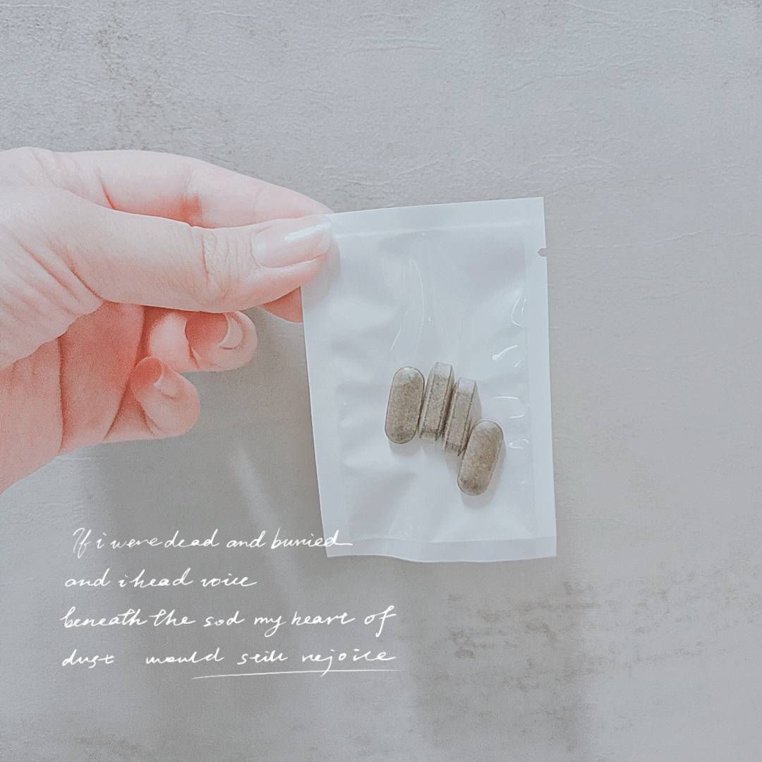 一手拿著一個白色小包，裡面裝著四顆棕色的藥丸狀物品，背景則是一面淺灰色的牆，牆上寫著詩句。