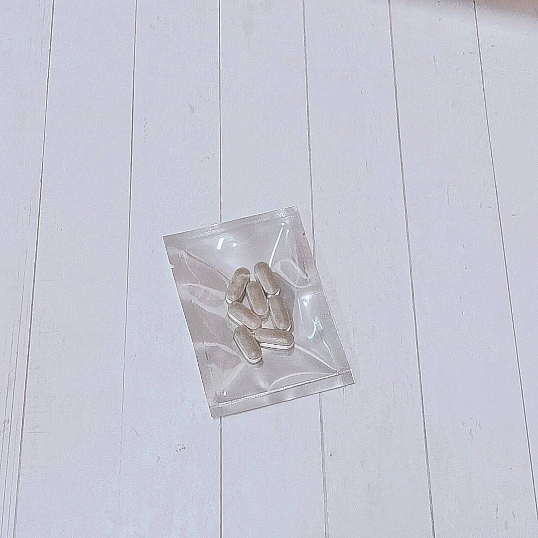 一隻手拿著一個銀色的小密封箔袋，裡面裝著幾片棕褐色的長方形藥片，背景是灰色。