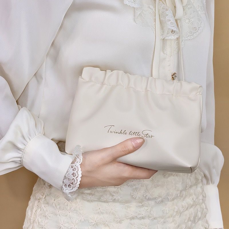 一隻手將一個有紋理的金色錐形物體放入一個標有“一閃一閃小星星”的米色束口袋中。