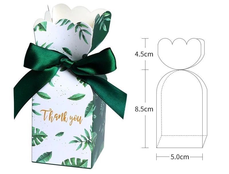 一個印有熱帶樹葉圖案和金色「謝謝」字樣的長方形禮盒，繫著深綠色絲帶，裡面裝著巧克力。