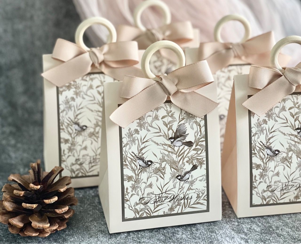 一個米色禮盒，印有鳥類圖案，繫著棕褐色絲帶蝴蝶結，放在一個白色華麗的裝飾盤上。